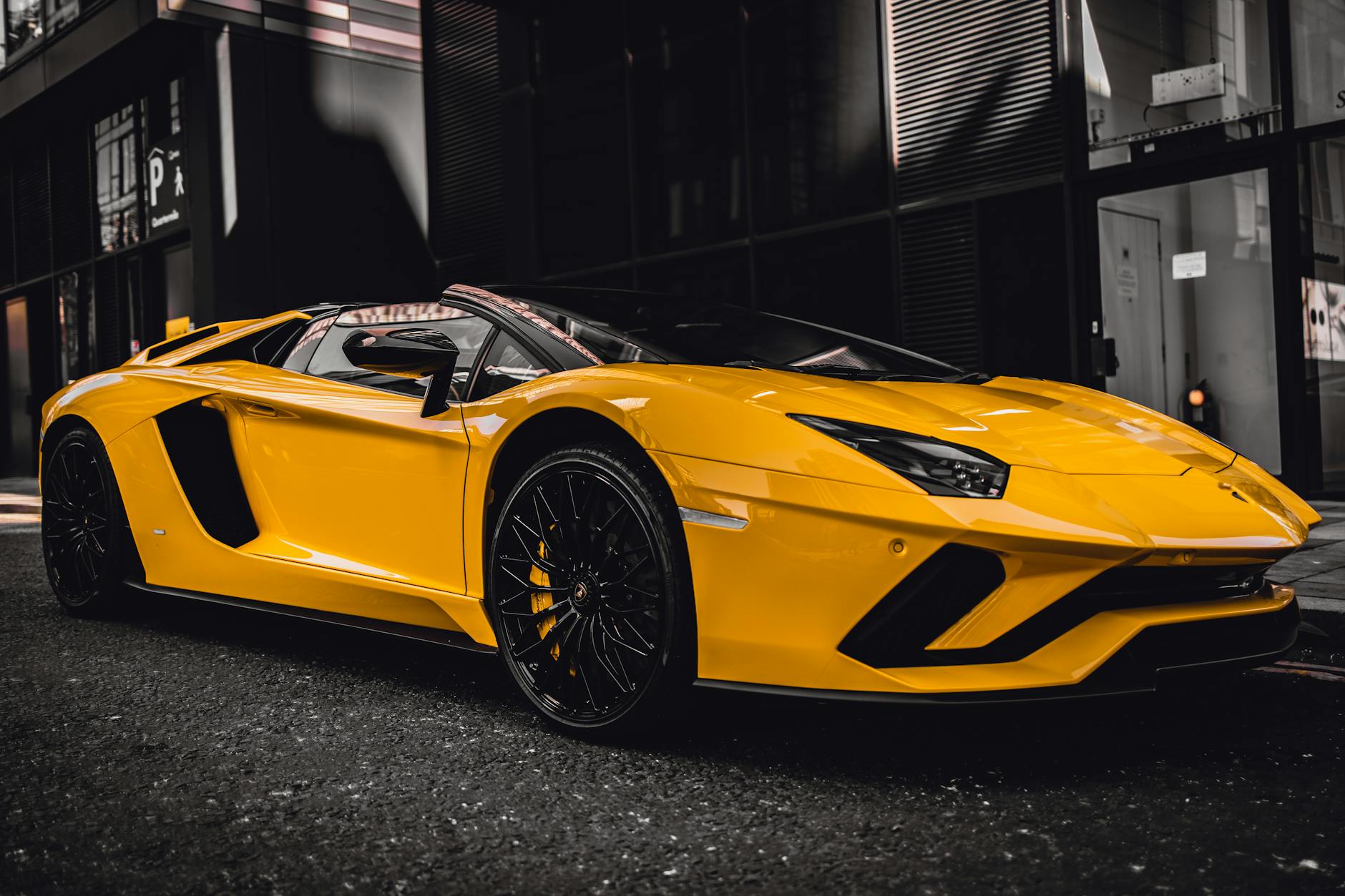 a yellow convertible luxury car parked beside black building